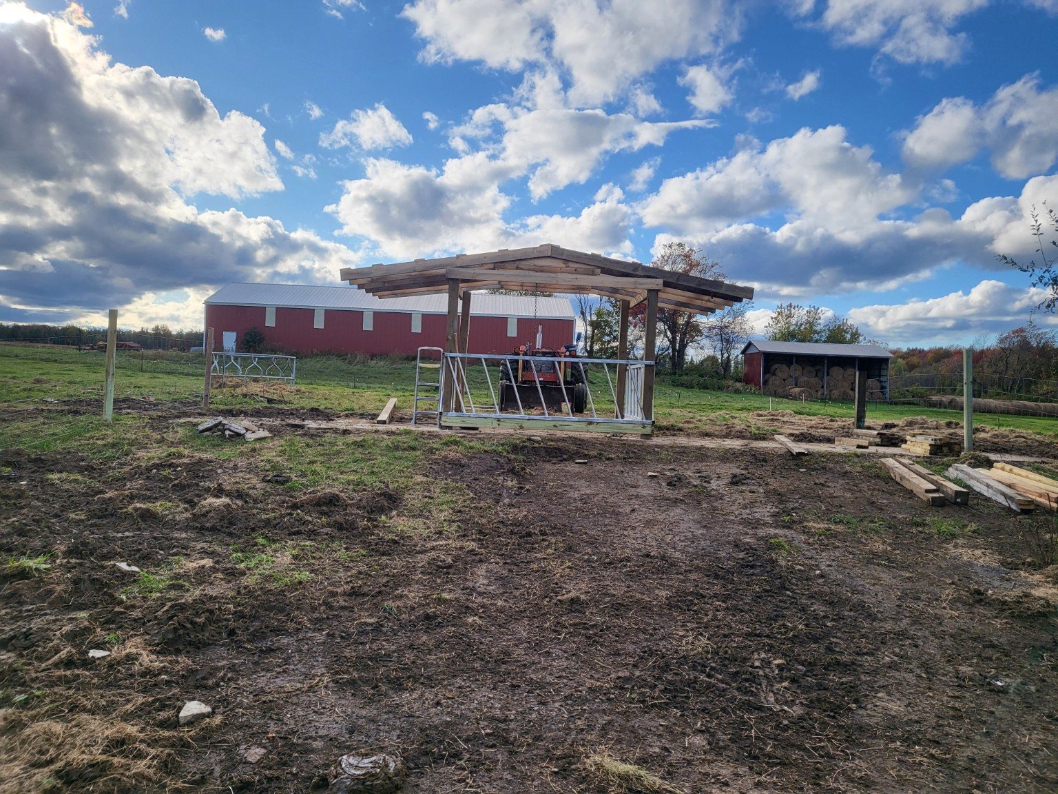 A wide view of a farm construction project with red barn and hay storage