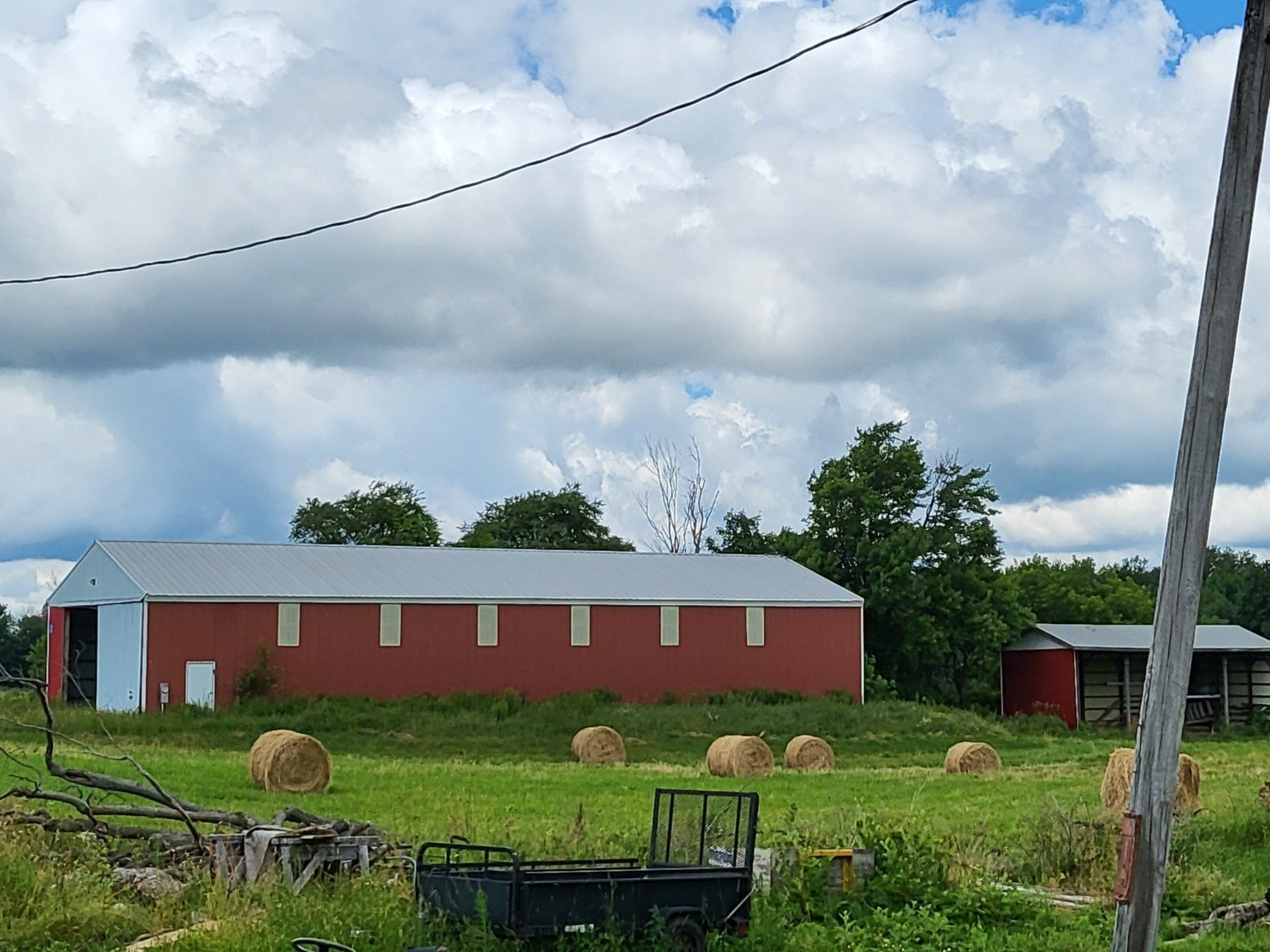 Round hay bales in the field with the red barn behind them