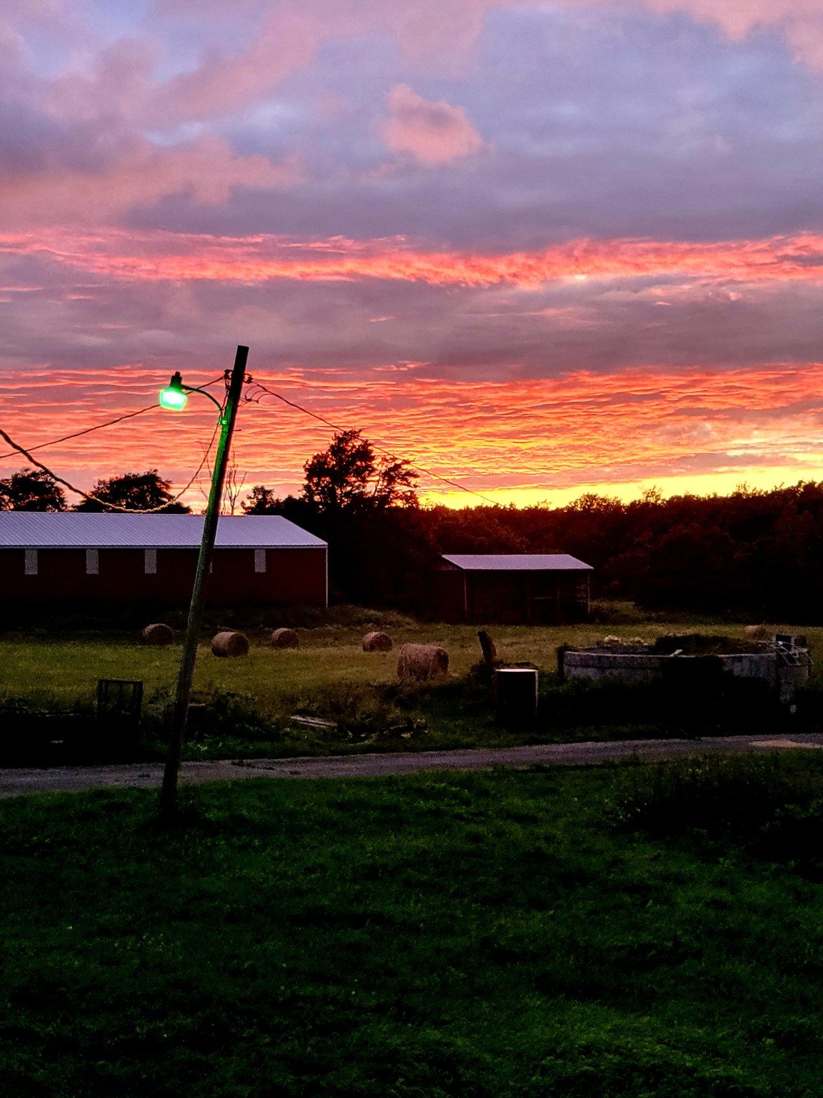 A vivid sunset over the farm and hay bales