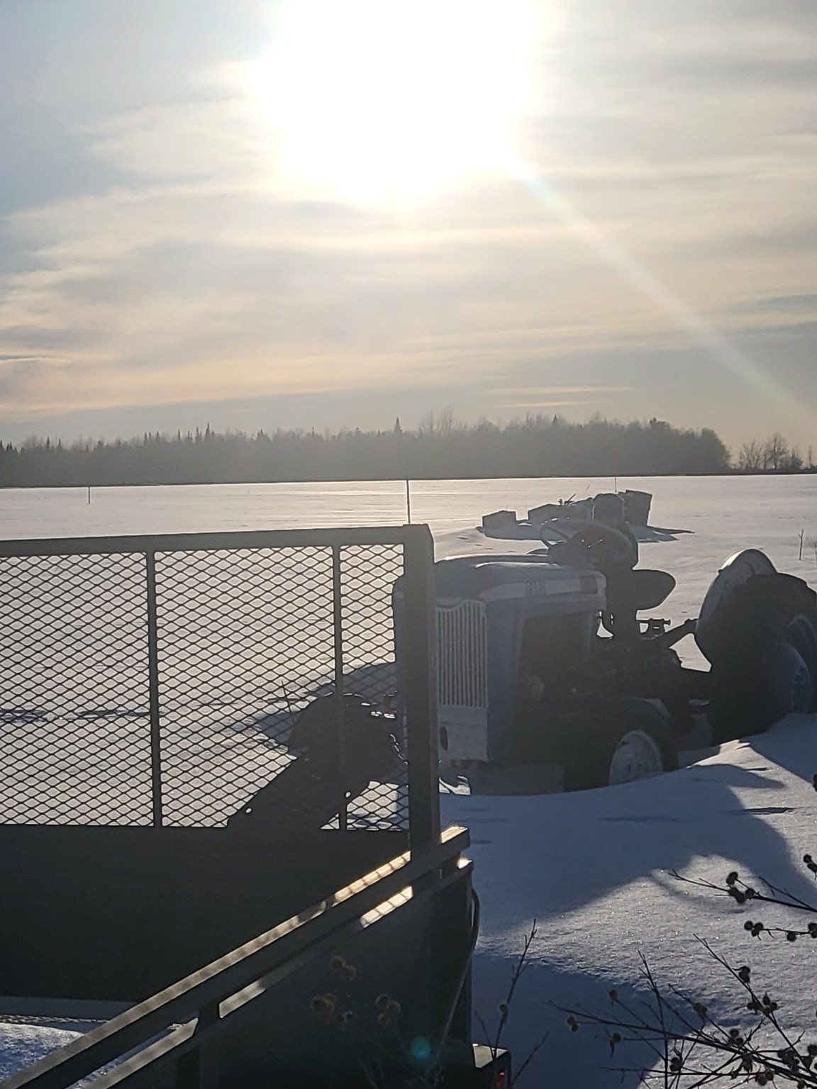 Farm equipment silhouetted against a bright winter field